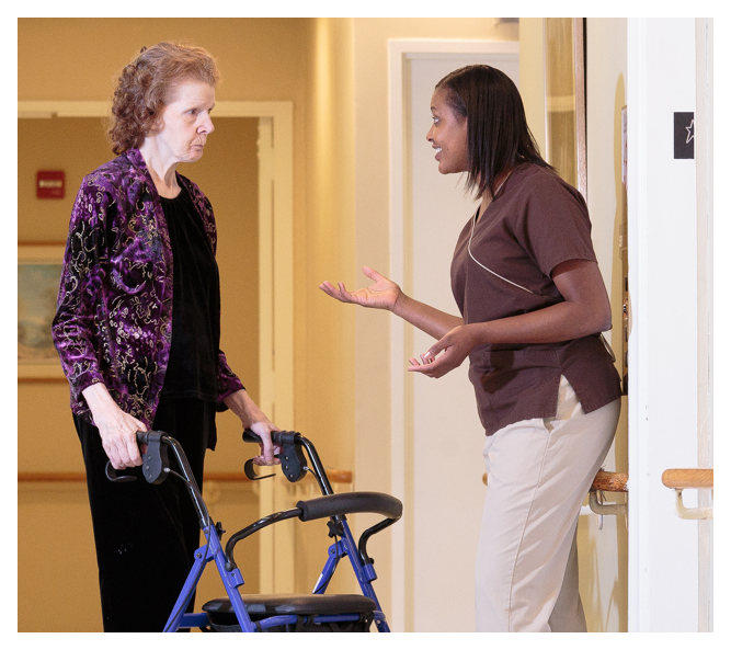 A friendly registered nurse chats to a senior resident using a rollator.
