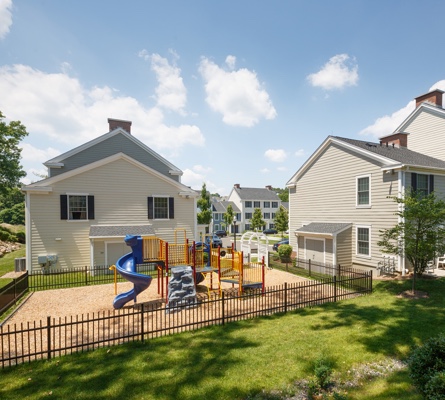 A sunny, outdoor communal area features a colorful playscape suitable for children near well-kept apartment buildings.