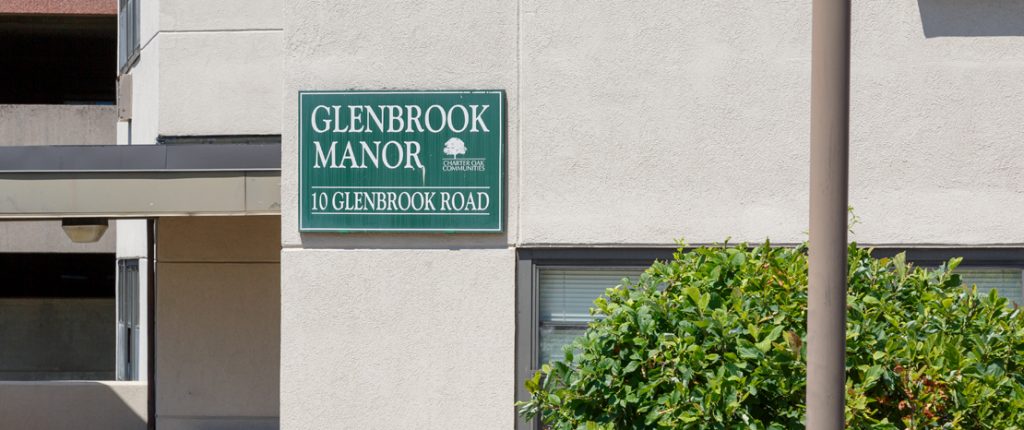 The square sign for Glenbrook Manor sits on the side of the concrete building and reads Glenbrook Manor, 10 Glenbrook Road.