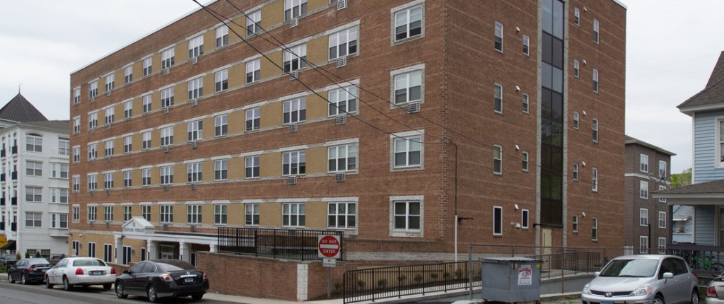 This view of the brick building shows a wheelchair accessible ramp, operable windows, and in-wall AC units.