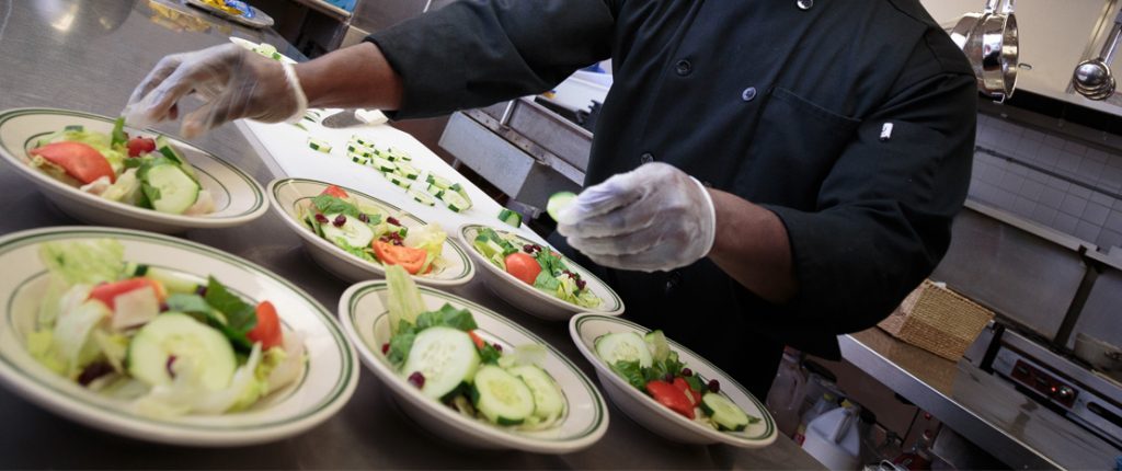 The on-site chef prepares six garden salads filled with fresh lettuce, wedge tomatoes, cucumbers, and more.