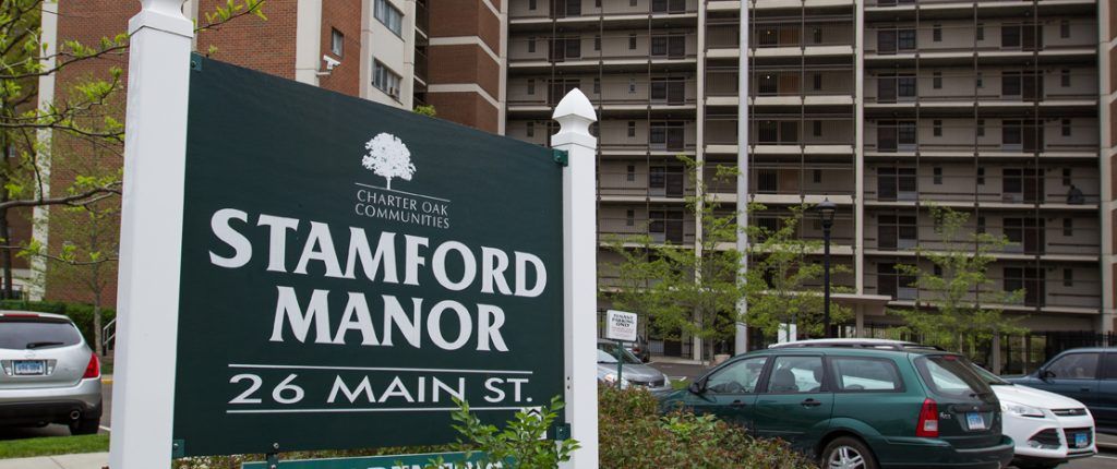 The sign for Stamford Manor sits amongst shrubbery and reads Stamford Manor, 26 Main St.