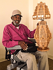 Clinton Manor resident Johnny Taylor sits in his motorized wheelchair, smiling while showing a unique, wooden lamp.